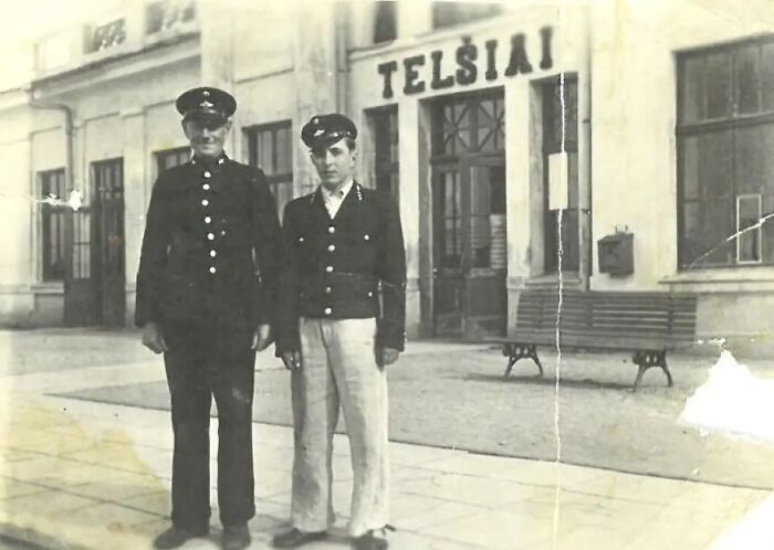 Two men in uniform standing outside a building, capturing life in Europe 100 years ago in a vintage photo.