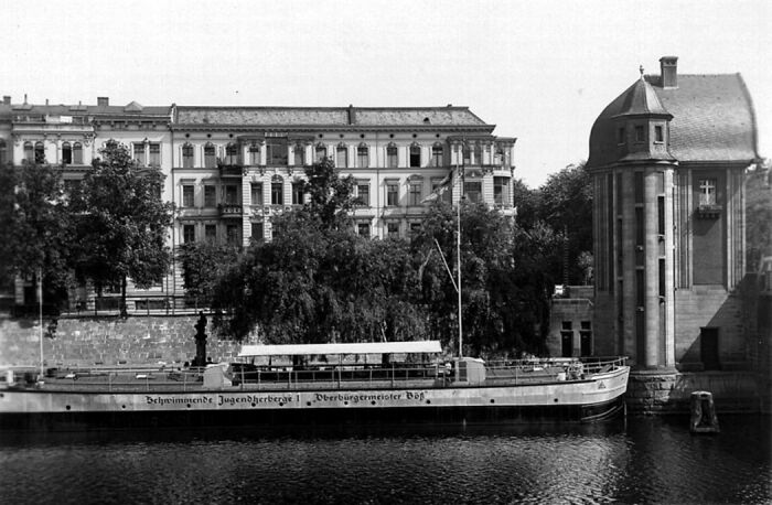 Boat docked by historic European riverside buildings showing life in Europe 100 years ago in black and white photo.