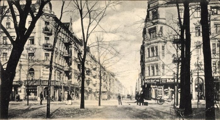 Vintage black and white photo showing street life in Europe with old buildings and leafless trees from 100 years ago.