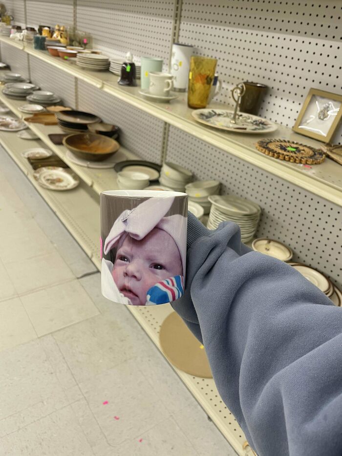 Goodwill hidden gem: a hand holds a mug with a baby's photo, shelves of ceramics in the background.