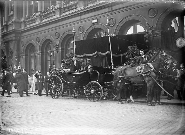 Black and white photo showing life in Europe 100 years ago with a horse-drawn carriage and people dressed in early 20th century attire.