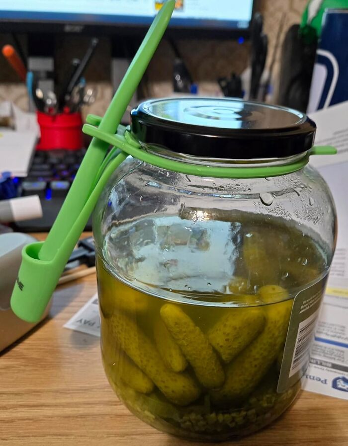 Jar of pickles with a green pickle grabber, a trendsetting kitchen treasure on a desk.