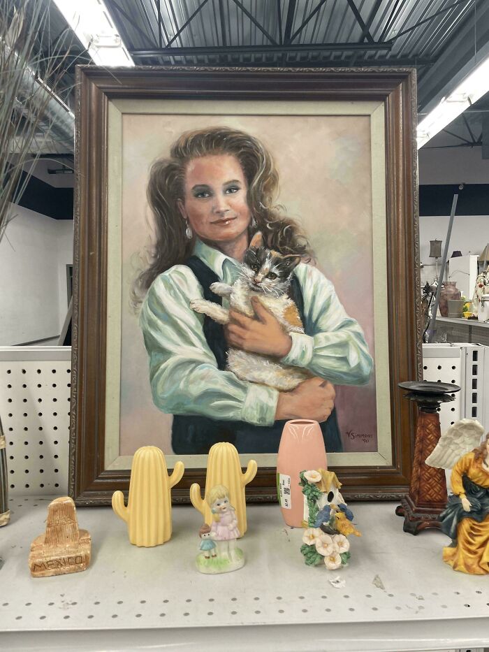 A portrait of a person holding a cat, found as a hidden gem at Goodwill, surrounded by various knick-knacks.