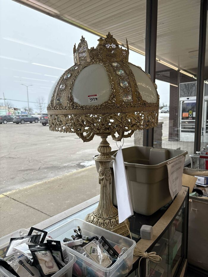 Ornate vintage lamp with intricate details, a surprising Goodwill gem, displayed on a store counter near assorted items.