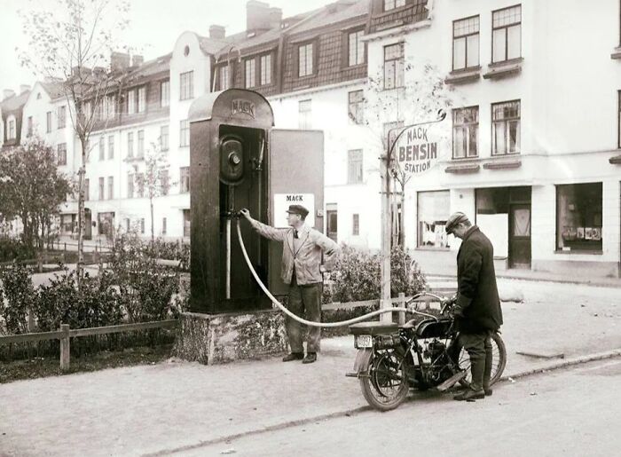 Vintage black and white photo of a man refueling a motorcycle at a Mack bensin station in Europe.