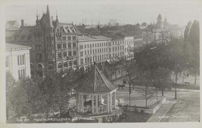 Black and white photo showing European city street with historic buildings and a music pavilion from 100 years ago.