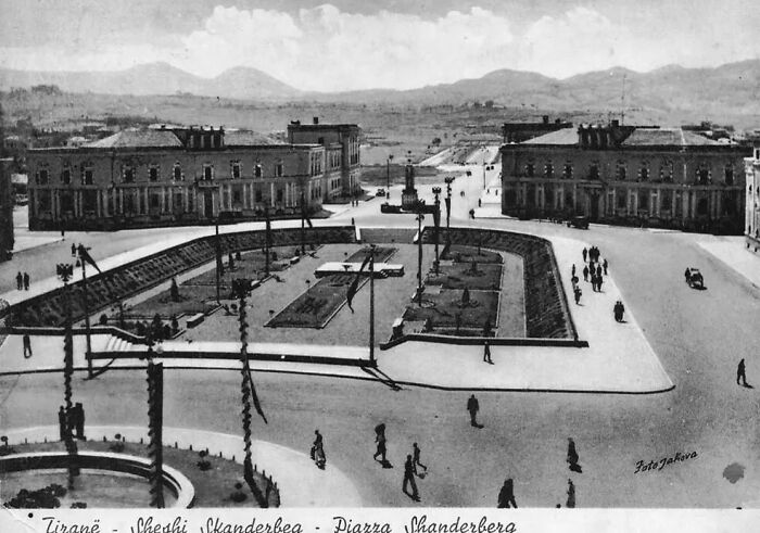 Black and white photo showing life in Europe 100 years ago with a central square and people walking around buildings.