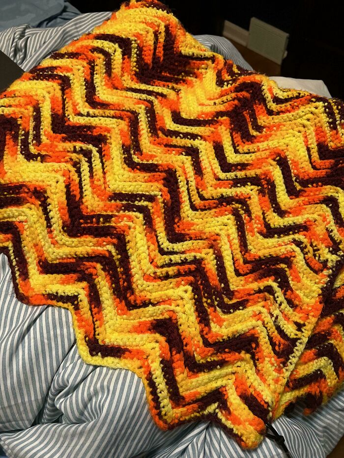 A colorful zigzag knit blanket found as a hidden gem at Goodwill, featuring orange, yellow, and brown patterns on a striped background.