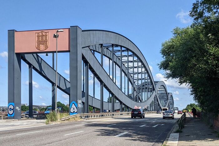 Impressive steel bridge with intricate curves, a lesser-known architectural wonder under a clear blue sky, vehicles passing.