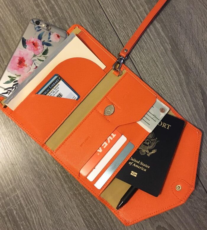 Orange travel wallet with passport, cards, and smartphone, ideal for budget-friendly vacation planning.