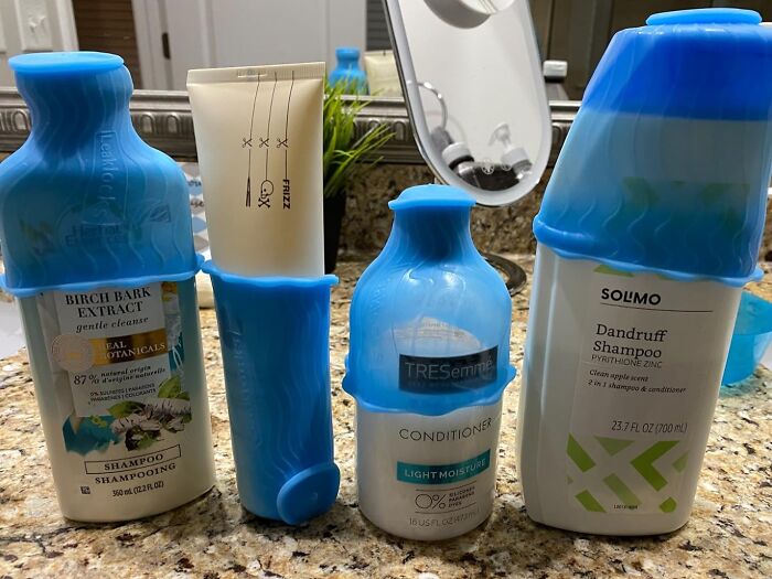 Travel essentials set with blue silicone covers on shampoo, conditioner, and lotion bottles on a bathroom counter.