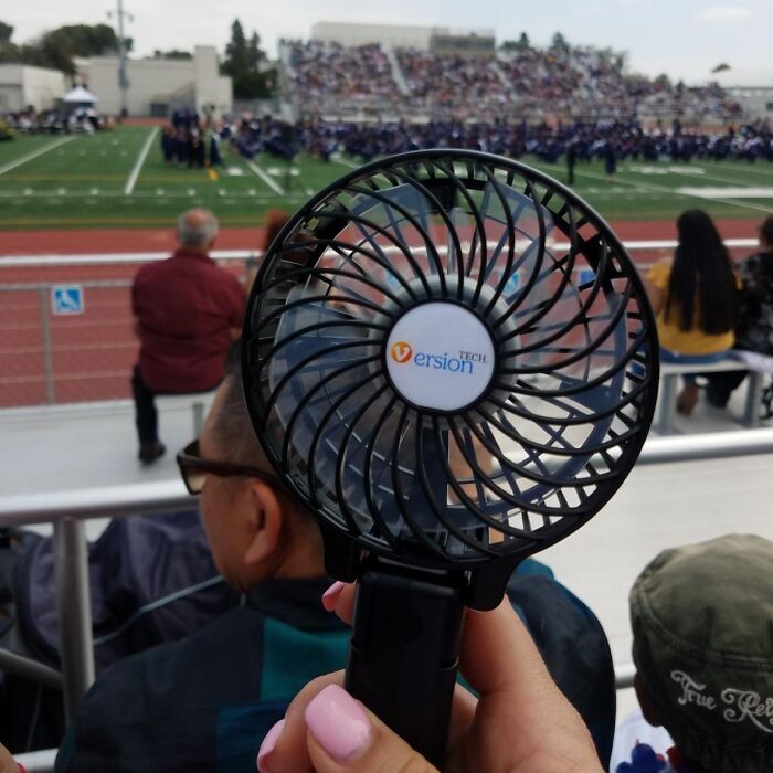 A portable fan held by a spectator at an outdoor event, showcasing a budget-friendly travel accessory.