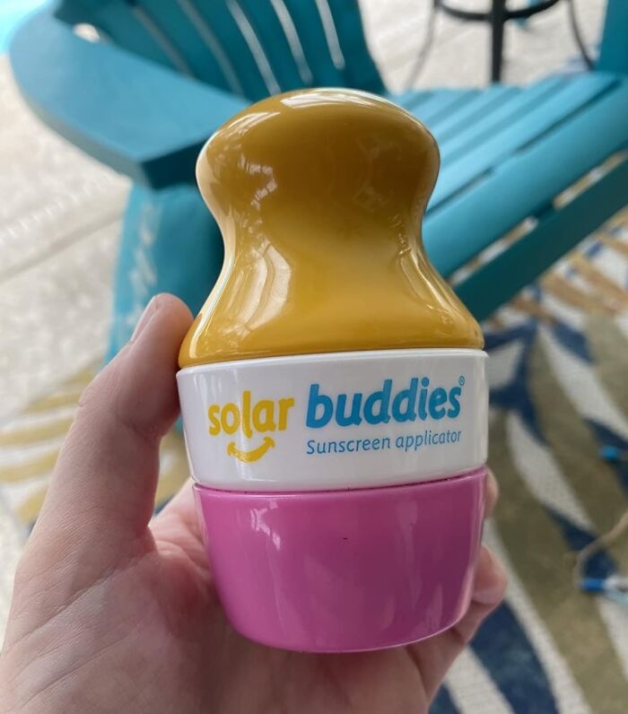 Affordable travel gadget: Solar Buddies sunscreen applicator, pink and yellow design, held in hand.