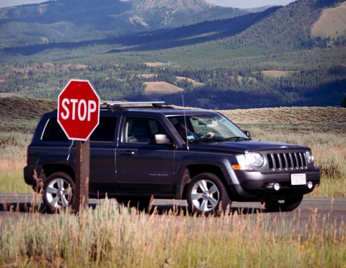 Black SUV stopped at a stop sign on a rural road with mountains in the background, illustrating unfortunate lottery stories.