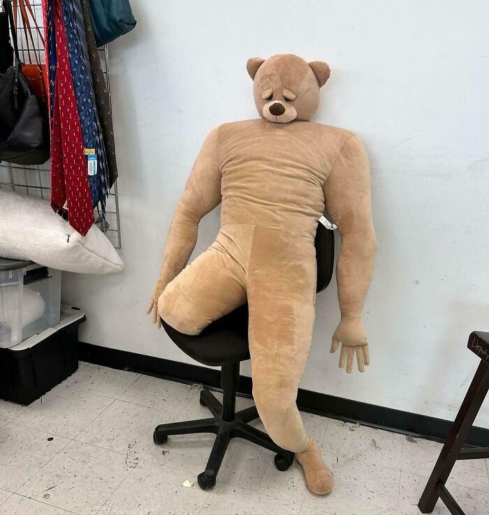 Bizarre item at Goodwill: oversized plush bear with a human-like body slumped on a chair, surrounded by clothing items.