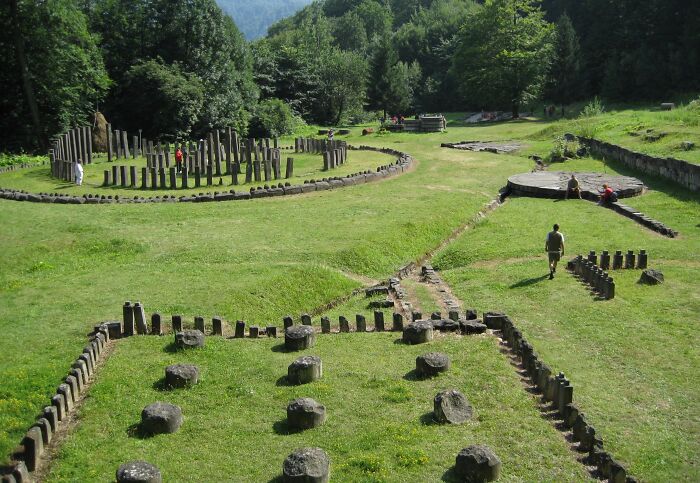 Unknown architectural wonders featuring ancient stone structures in a grassy landscape surrounded by trees.