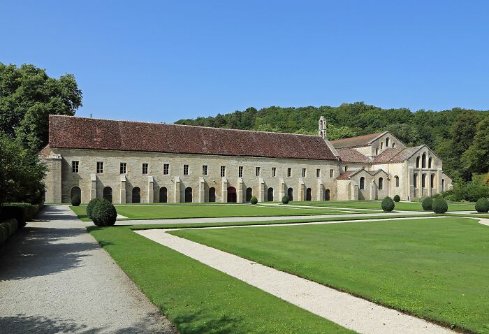 Historic architectural wonder with arched stone facade and manicured lawns, set against a wooded backdrop.