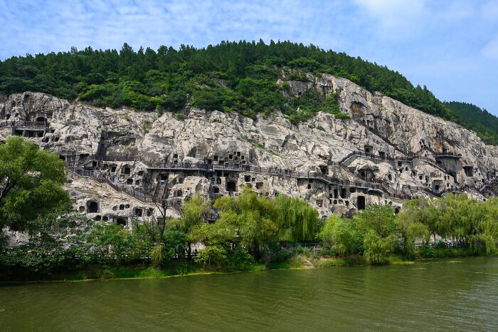 Rock-carved architectural wonders in a lush green landscape by a river, showcasing intricate historical craftsmanship.