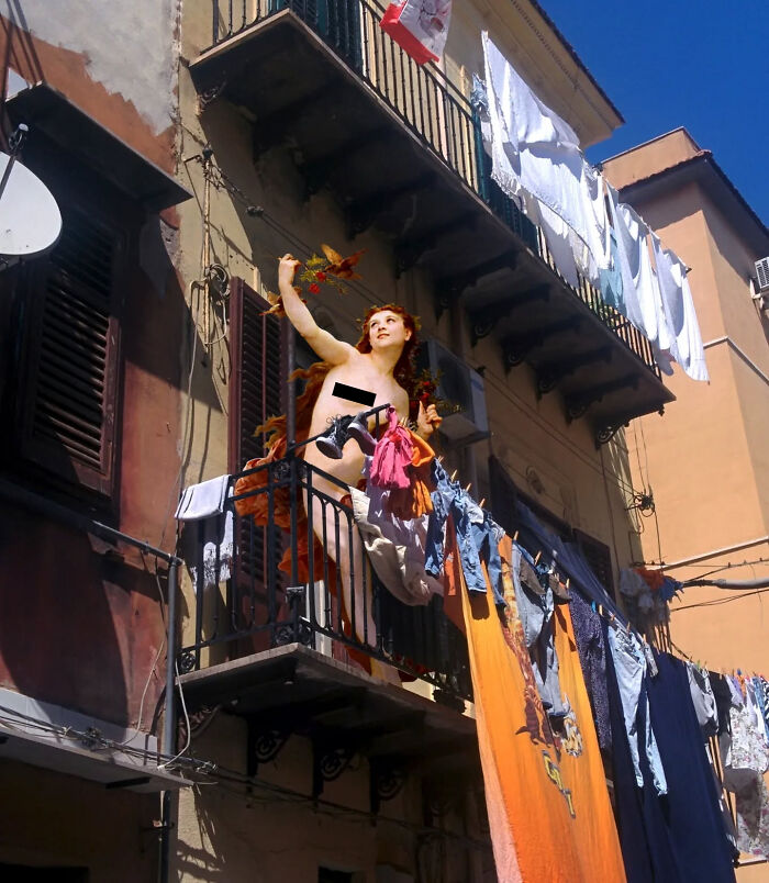 Classical figure on a balcony amidst modern laundry, blending past and present.
