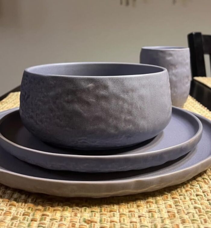 Set of textured ceramic bowl, plates, and cup arranged on woven placemat, ideal Mother's Day gifts for a unique reaction.