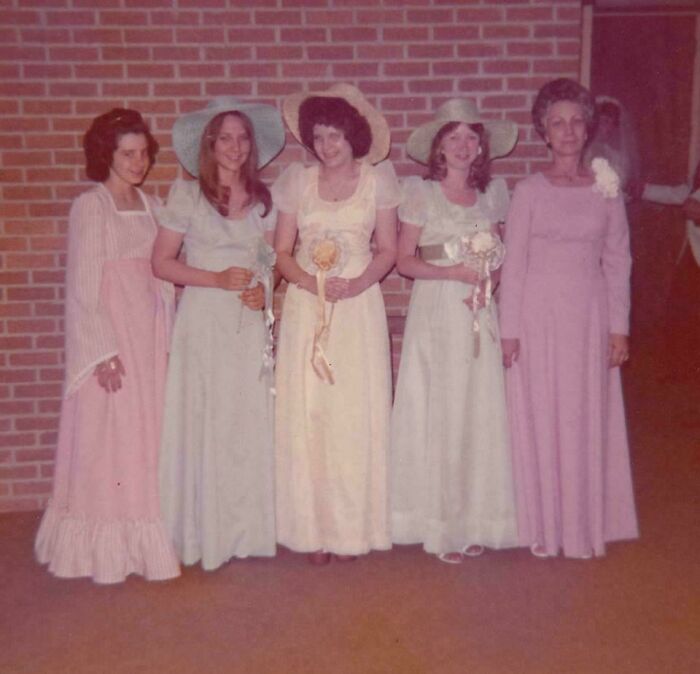 Five women in vintage dresses and hats standing together, evoking the past with an old photograph charm.