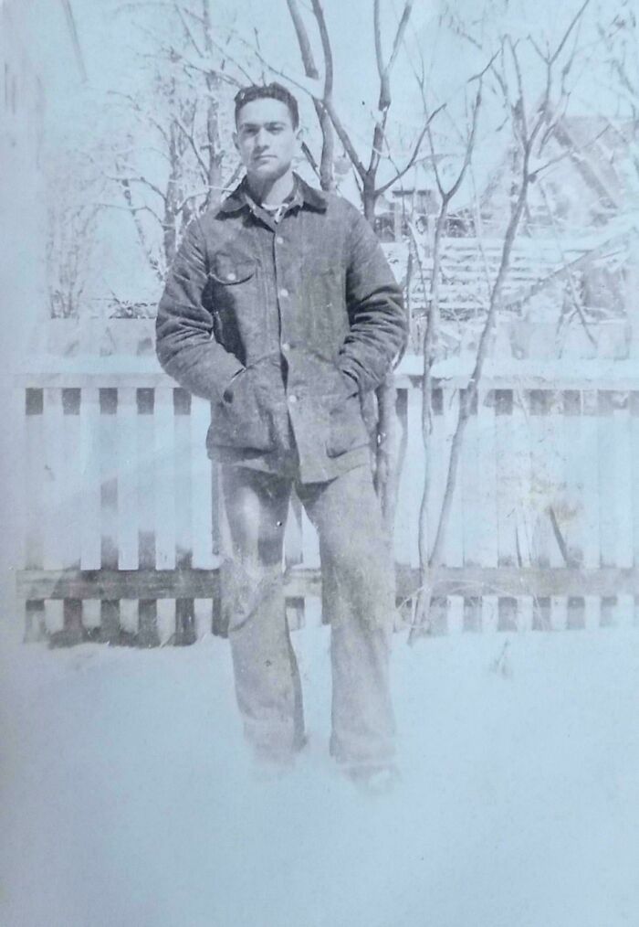 A man in a winter coat stands in a snowy, vintage setting, conveying beautiful old-fashioned charm.