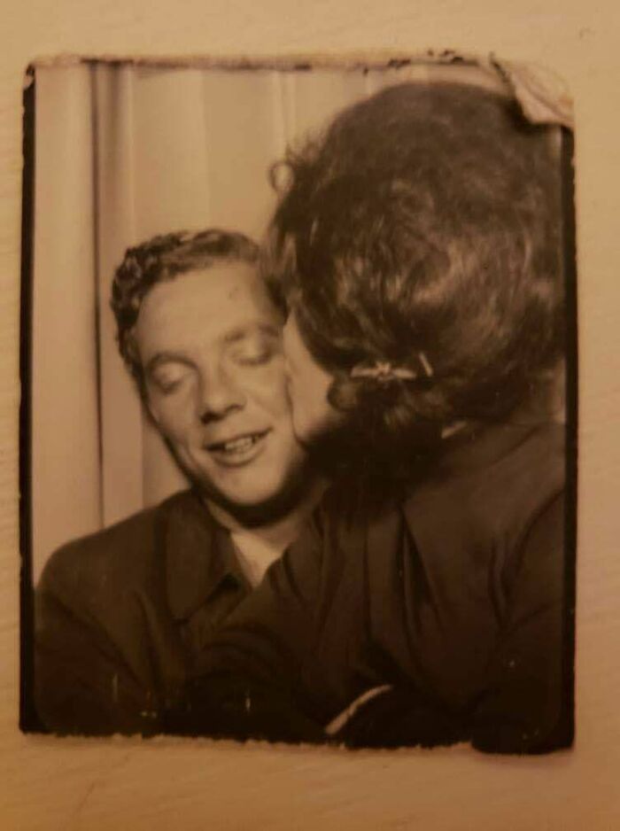 A nostalgic old photo showing a woman kissing a smiling man on the cheek, capturing a beautiful moment from the past.
