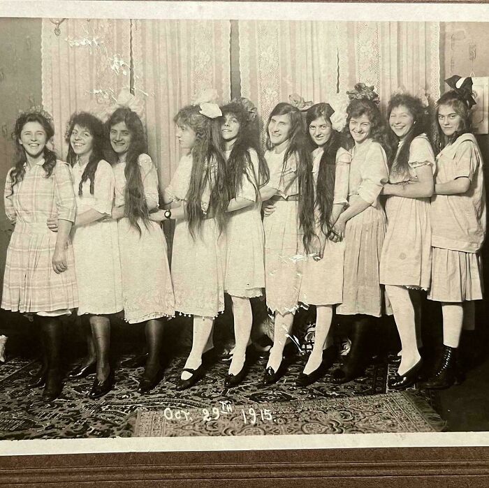 Vintage photo of nine smiling girls with long hair and bows, taken in 1915, showcasing beautiful moments from the past.