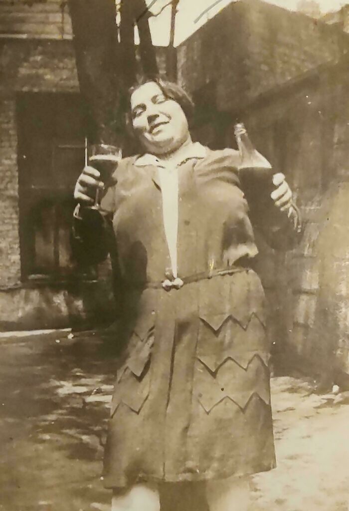 A woman holding drinks and smiling outdoors in a vintage setting, capturing an interesting moment from the past.