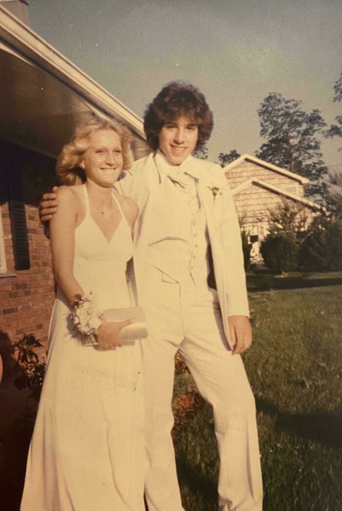 Young couple dressed for prom in vintage attire, standing outside a house, capturing a beautiful moment from the past.