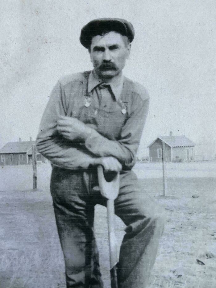 A man in vintage workwear leans on a shovel, embodying the essence of beautiful and interesting old photography.