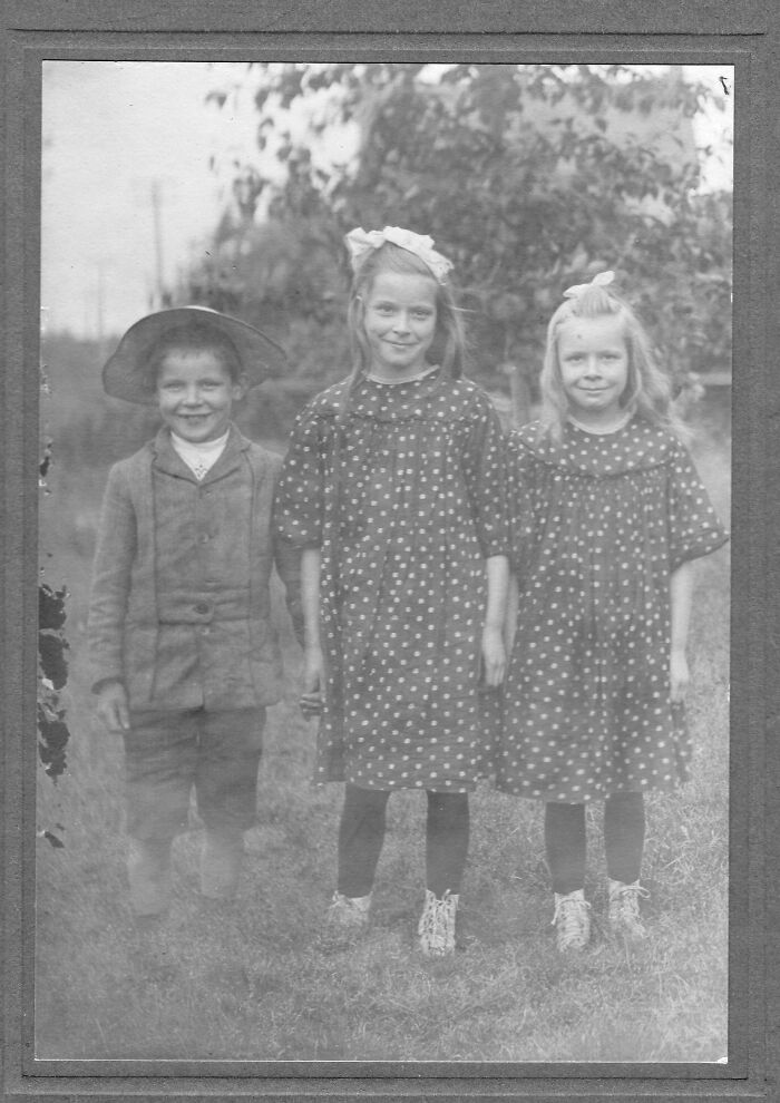 Vintage photo of three smiling children in old-fashioned attire, capturing a glimpse of the past.