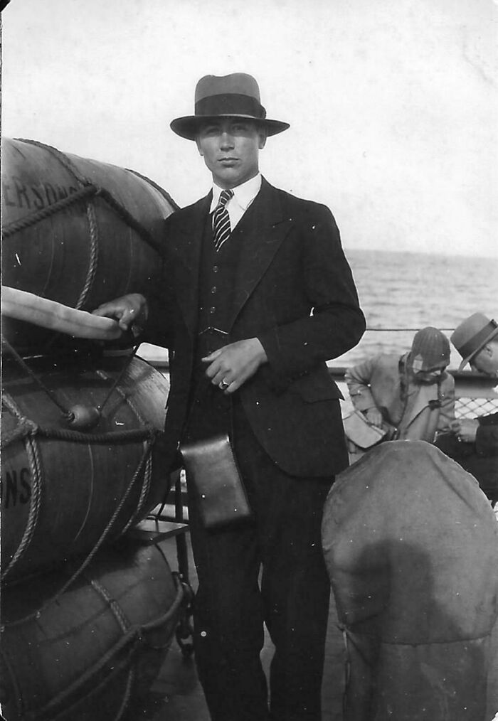 A man in a suit and hat poses next to lifebuoys on a ship deck, capturing a moment from the past.