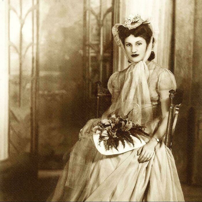 A woman in vintage attire holding a bouquet, capturing a moment from the past.