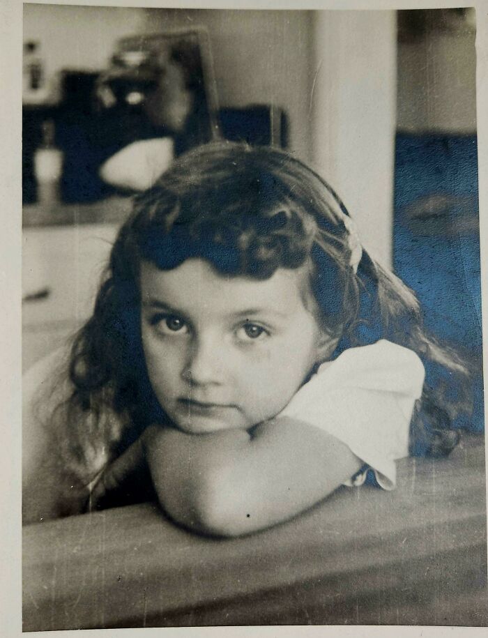 Vintage photo of a young girl with curly hair, lying on her arms, bringing the past to life.