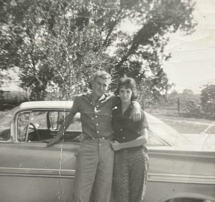 A couple posing by a vintage car, capturing a beautiful and interesting moment from the past.