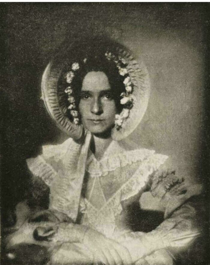 Old photograph of a woman in Victorian attire with floral bonnet, showcasing historical fashion.