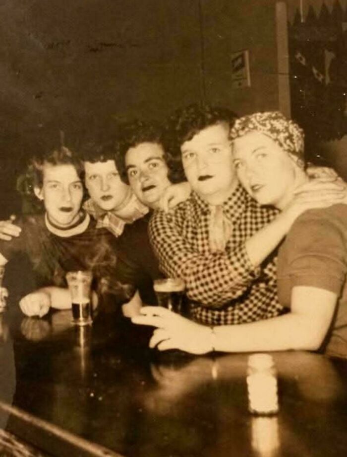 A group of people sitting at a bar table with drinks, captured in an old, beautiful and interesting photo.