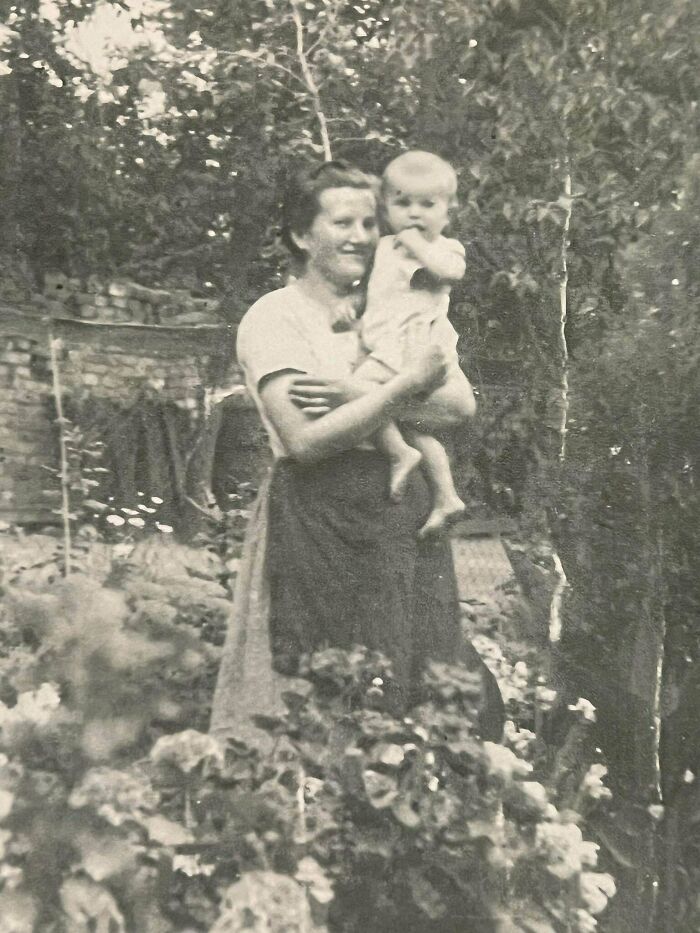 Vintage photo of woman holding a baby in a lush garden, capturing a beautiful moment from the past.