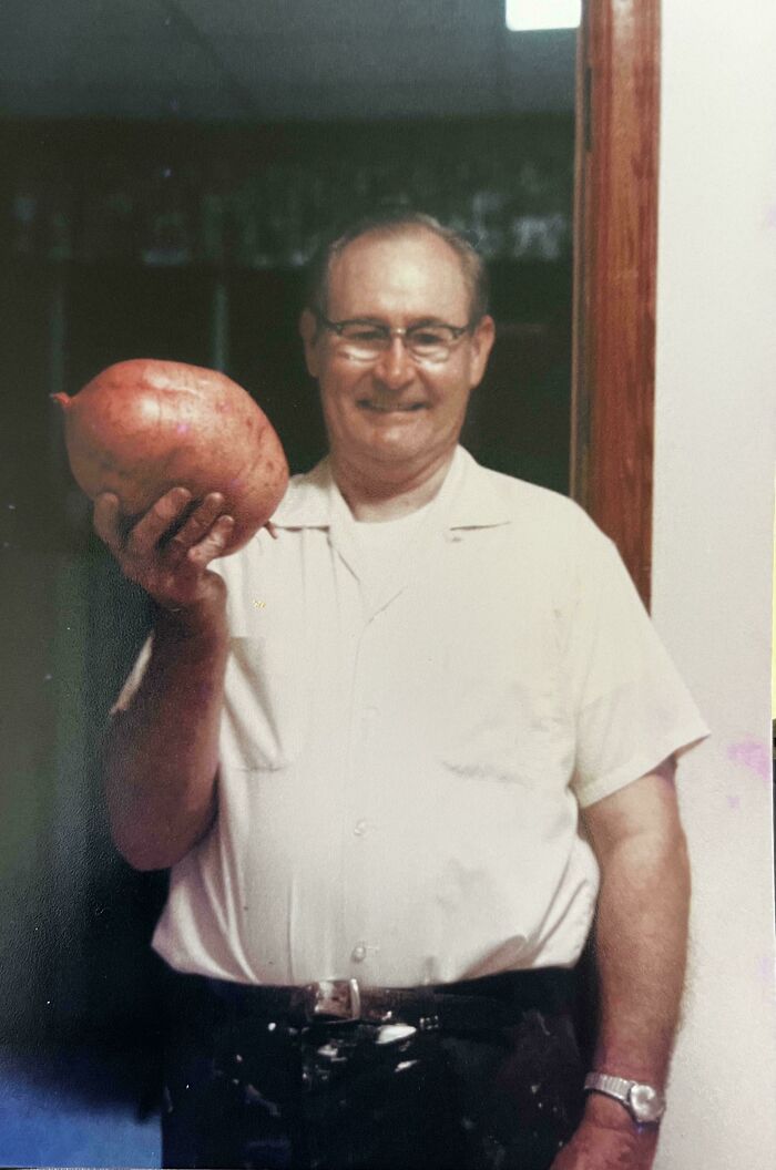 Man holding a large vegetable, smiling in a vintage photo capturing a moment from the past.