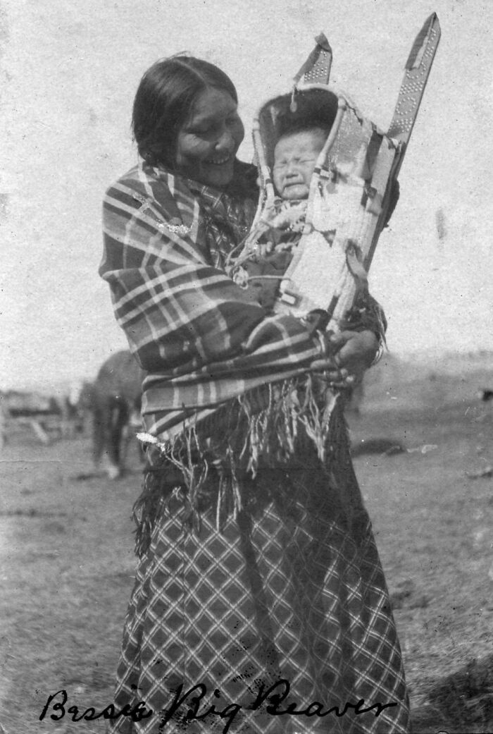 Native American woman holding a baby in a traditional cradleboard, revealing real lives from a century ago.