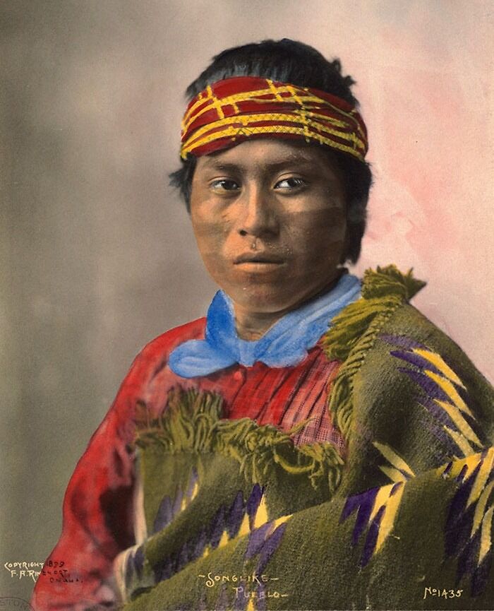 Native American man from a century ago wearing traditional Pueblo clothing and a colorful headband in a haunting historic photo.