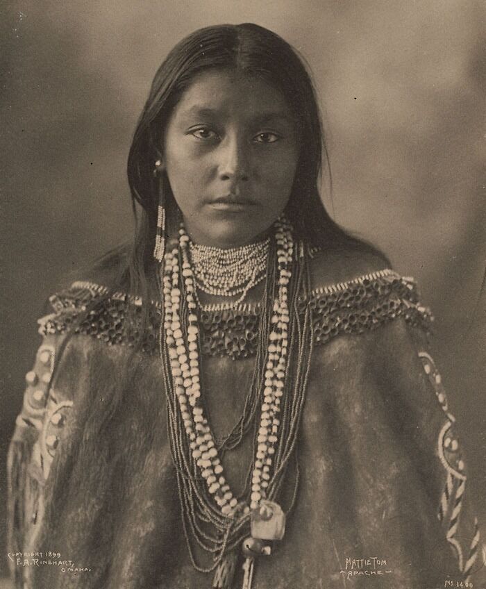 Portrait of a Native American woman wearing traditional beaded clothing and jewelry in a historic haunting photo.