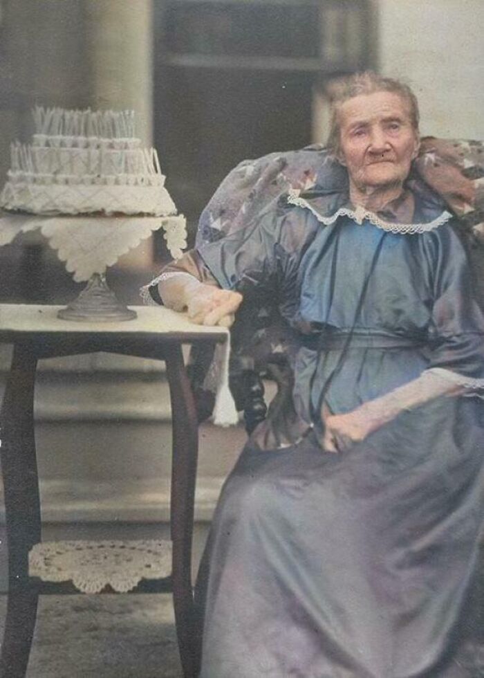 Mujer mayor sentada junto a una torta de cumpleaños con muchas velas, imagen histórica elocuente de décadas atrás.