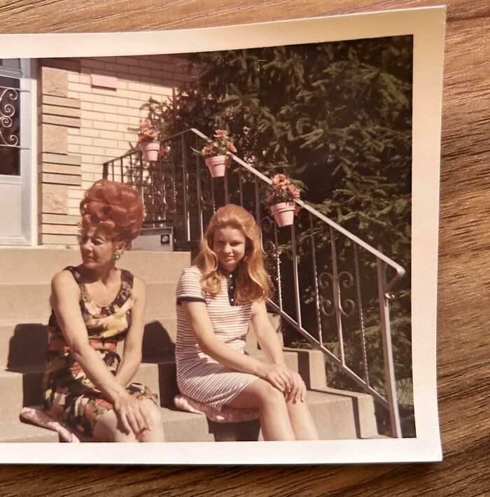 Two women sitting on steps in the past, adorned with floral dresses and surrounded by flowers.