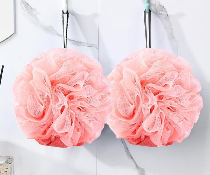 Two pink bath poufs hanging on hooks against a white tiled wall, popular Amazon haul finds for bath accessories.