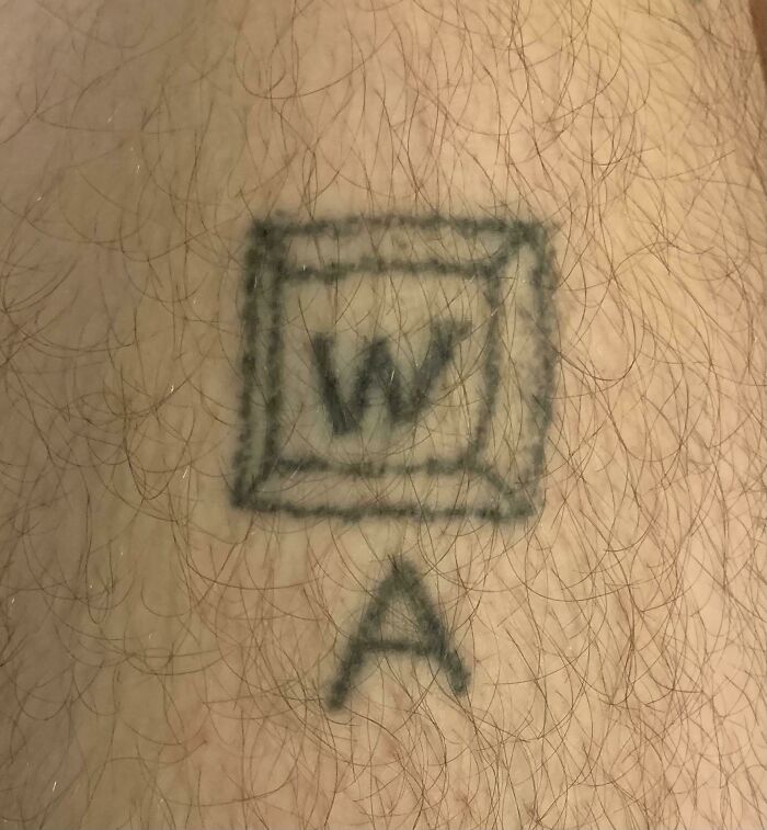 Faded tattoo fail showing a poorly drawn 3D box with the letter W and a separate letter A on hairy skin.