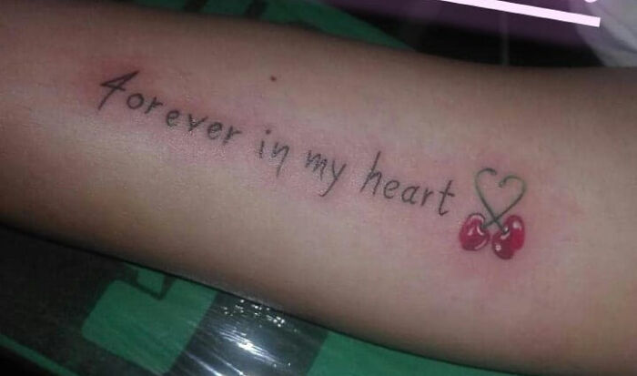Tattoo fail showing misspelled text forever in my heart with a heart-shaped cherry design on forearm.