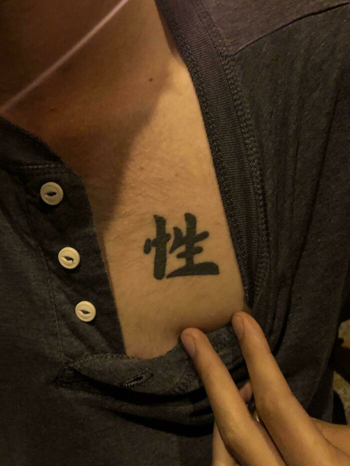 Close-up of a wild tattoo fail featuring a black ink symbol on the chest partially revealed by a dark shirt.