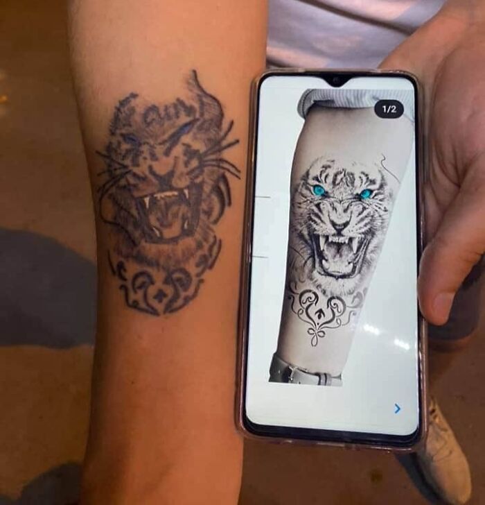 Tattoo fail of a tiger with blue eyes compared to the original detailed design shown on a smartphone screen.